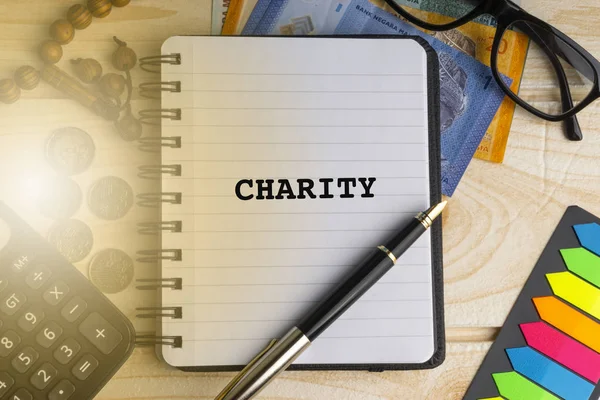 Sadaka kitabe üzerinde kitap yazılmış hesap makinesi, tespih, madeni para, banknot, kitap, gözlük ve ahşap arka plan üzerinde kalem. İş, sigorta ve İslam kavramı