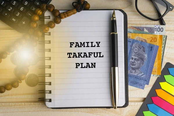 FAMILY TAKAFUL PLAN inscription written on book with calculator, rosary, coins, banknotes, book, eyeglasses and pen on wooden background. Business, Insurance and Islamic concept