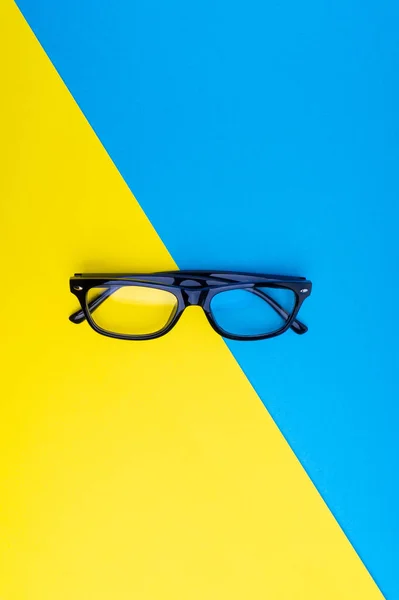 Black frame eyeglasses on blue and yellow background