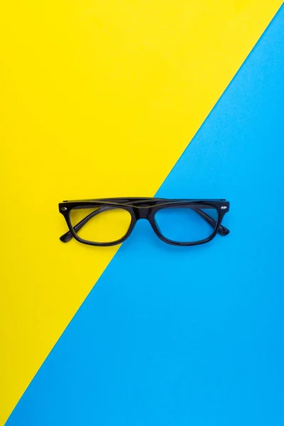 Black frame eyeglasses on blue and yellow background