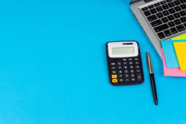 Düz yatıyordu, üst görünüm ofis masa masası. Hesap makinesi, siyah kalem, turqoise mavi arka planda dizüstü bilgisayar ile çalışma alanı. İş finansmanı, eğitim teknolojisi ve metin konsepti için Copy Space