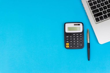 Düz yatıyordu, üst görünüm ofis masa masası. Hesap makinesi, siyah kalem, turqoise mavi arka planda dizüstü bilgisayar ile çalışma alanı. İş finansmanı, eğitim teknolojisi ve metin konsepti için Copy Space