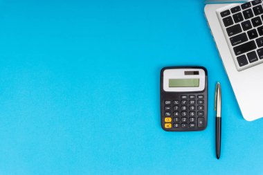 Düz yatıyordu, üst görünüm ofis masa masası. Hesap makinesi, siyah kalem, turqoise mavi arka planda dizüstü bilgisayar ile çalışma alanı. İş finansmanı, eğitim teknolojisi ve metin konsepti için Copy Space