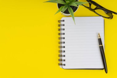 Ofis masa masasına bakın. Siyah kalem, Gözlük, dekorasyon çiçek ve sarı arka planda kitap ile çalışma alanı. İş, finans ve kopya alanı konsepti