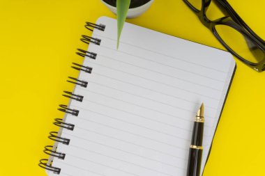 Ofis masa masasına bakın. Siyah kalem, Gözlük, dekorasyon çiçek ve sarı arka planda kitap ile çalışma alanı. İş, finans ve kopya alanı konsepti