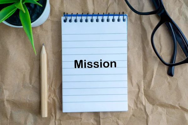 Not defteri, çiçek vazo, gözlük, kalem ve ahşap kağıt arka plan üzerinde misyon kelimeler. İş, eğitim kavramı ve kopyalama alanı kavramı