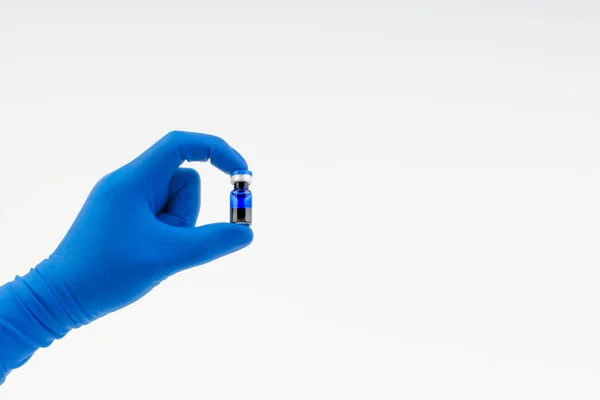 Beyaz üzerinde izole tıbbi şişe tutan mavi bir eldiven el