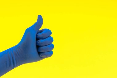 İşaret başparmakları yukarı veya sarı arka planda iyi mavi bir eldiven el