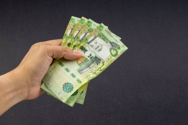 El siyah arka plan üzerinde Suudi Riyal banka notları tutarak. Finansal kavram ve seçici odak