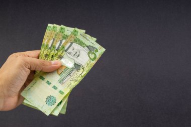 El siyah arka plan üzerinde Suudi Riyal banka notları tutarak. Finansal kavram ve seçici odak