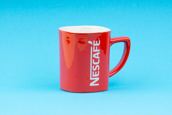 Kuala Lumpur, Malaysia - July 03, 2019:  Promotional red Nescafe mug on blue background. Selective focus