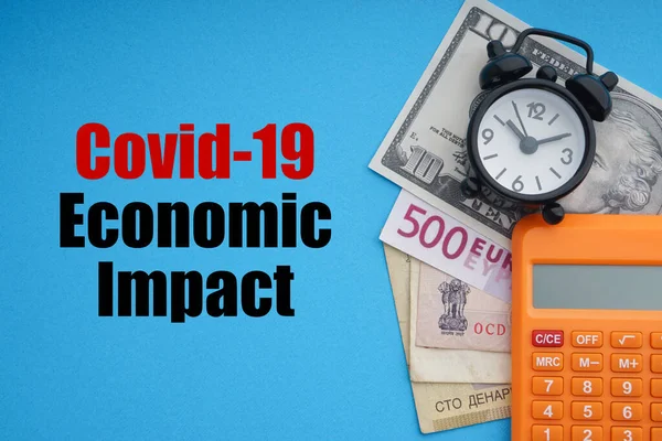 COVID19 ECONOMIC IMPACT text with alarm clock, banknotes currencies  and calculator on blue background. Coronavirus Covid19 and Business Concept