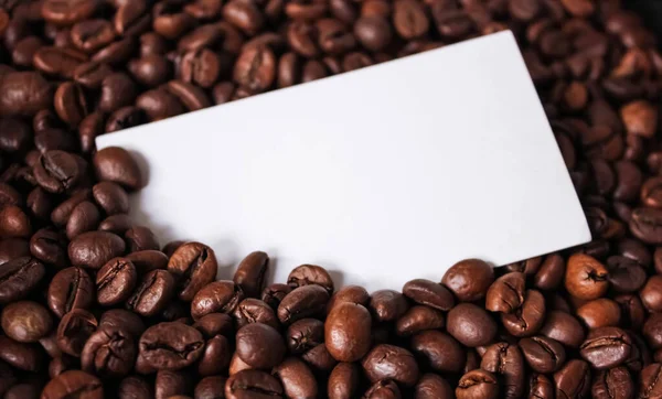 Blank white business card for your text, design, logo on coffee beans background close up photo. Concept mockup for logo design.