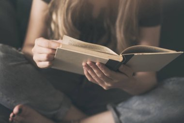 Kanepede kitap okuyan genç bir kadın.