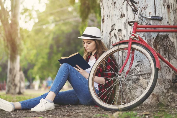 Kız ağaca karşı yaslanmış bir kitap okuma