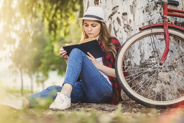 Kız ağaca karşı yaslanmış bir kitap okuma