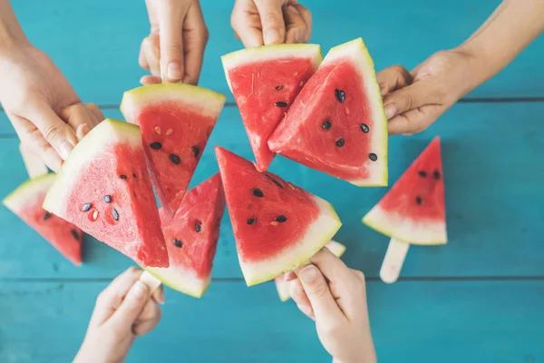 Hands raising watermelon popsicles on wooden background