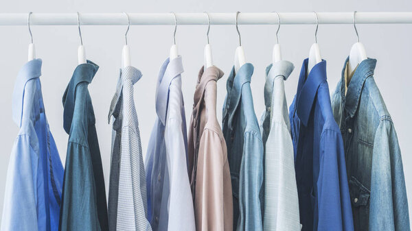 Голубые рубашки, висящие на деревянных вешалках
