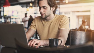 Genç adam kafede dizüstü bilgisayar kullanıyor.