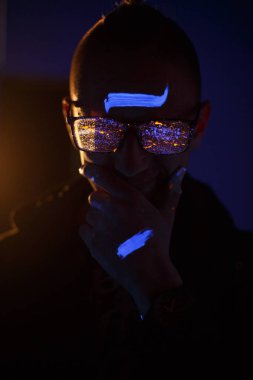 Karanlık bir odada biri. Gözlüklerini boya ile sıçrayan.