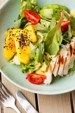 Ahşap arka plan üzerinde beyaz bir tabak üzerinde ızgara tavuk, mango, marul, avokado, domates, arugula, peynir sause ile Salata