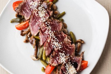 Turşu ile dilimlenmiş orta nadir Rosto sığır eti, kiraz domates, ahşap arka plan üzerinde beyaz bir tabak üzerinde mantar.