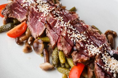 Turşu ile dilimlenmiş orta nadir Rosto sığır eti, kiraz domates, ahşap arka plan üzerinde beyaz bir tabak üzerinde mantar.