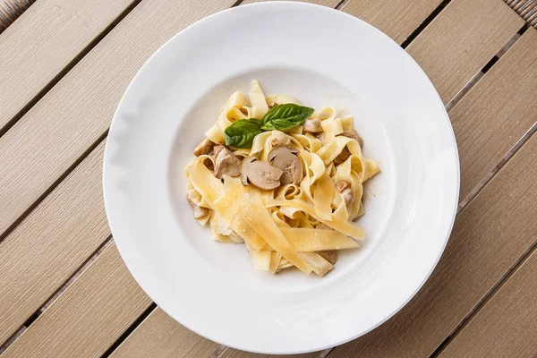 Tagliatelle vegetarian Pasta Dish with Mushrooms decorated with basil. Delicious lunch with pasta and white mushrooms. On wooden background.
