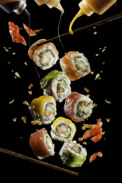Flying pieces of sushi with wooden chopsticks and sauce, isolated on black background. Flying food and motion concept. Very high resolution image