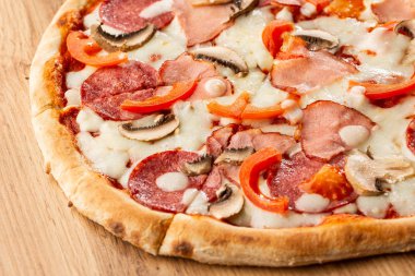 Ahşap masa üzerinde lezzetli Capricciosa Pizza üst görünümü. Malzemeler soyulmuş domates, peynir, jambon, mantar, salam.