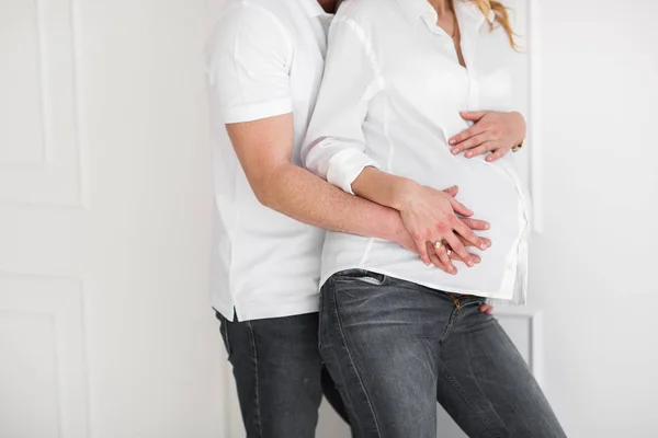 Vacker gravid kvinna med stilig man håller händerna på magen i vardagsrummet. — Stockfoto