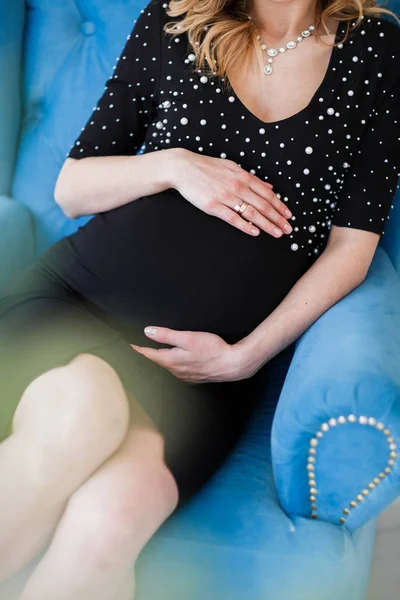 Femme enceinte en robe noire tient la main sur le ventre sur un fond blanc . — Photo