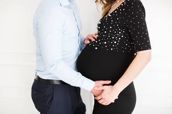 Vacker gravid kvinna med stilig man håller händerna på magen i vardagsrummet. — Stockfoto