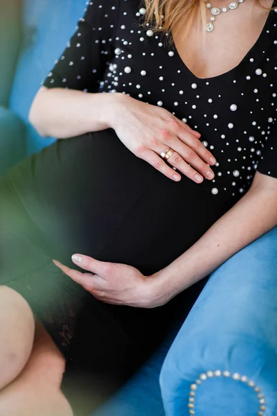 Femme enceinte en robe noire tient la main sur le ventre sur un fond blanc . — Photo