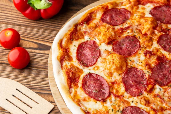 Delicious hot homemade Pepperoni pizza on the wooden table. Pepperoni Pizza - Fresh homemade pizza with pepperoni, cheese and tomato sauce on rustic black stone background with copy space.