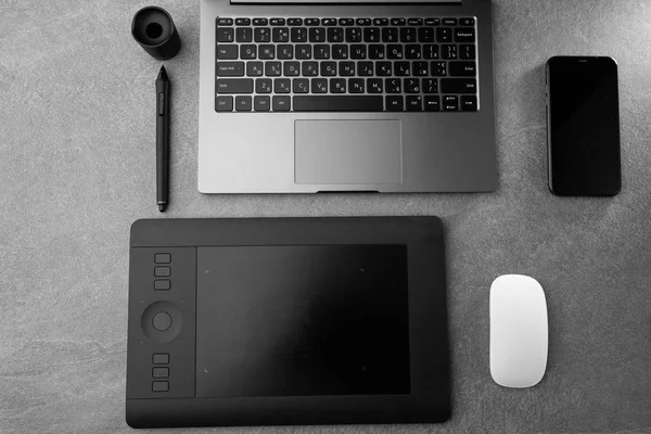 Χώρος εργασίας με ανοιχτό φορητό υπολογιστή με μαύρη οθόνη, ποντίκι, tablet γραφικών και έξυπνο τηλέφωνο σε μοντέρνο γκρι πέτρινο γραφείο, γωνιακό σημειωματάριο στο τραπέζι, τραπέζι γραφείου με σημειωματάριο, υπολογιστή. αντίγραφο χώρου. οριζόντια — Φωτογραφία Αρχείου