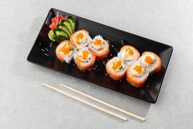 Somon, avokado, krem peynir ve kırmızı havyarlı Philadelphia usulü suşi. Suşi menüsü. Kara tabakta. Geleneksel Japon deniz ürünleri, sağlıklı gıda konsepti. Beyaz arkaplanda üst görünüm yatay fotoğraf.