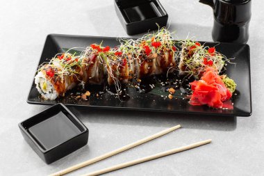 Philadelphia suşisi, yılan balığı, avokado, krem peynir ve havyar. Suşi menüsü. Beyaz arka planda, koyu taştan bir tabakta. Geleneksel Japon deniz ürünleri, sağlıklı gıda konsepti. Yatay fotoğraf.