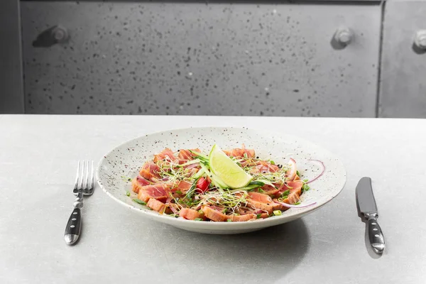 Az pişmiş ton balığı dilimlerini limon ve roka yapraklarıyla kaplayın. Gri arka plan. Ton balığı salatası. Yukarıdan yatay görünüm.