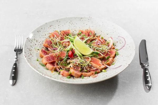 Az pişmiş ton balığı dilimlerini limon ve roka yapraklarıyla kaplayın. Gri arka plan. Ton balığı salatası. Yukarıdan yatay görünüm.