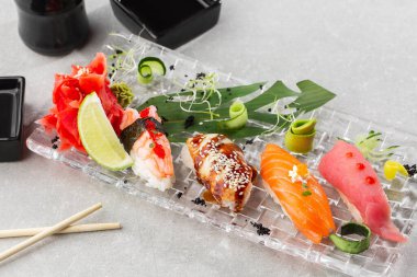 Şeffaf tabakta servis edilen somon, yılan balığı, ton balığı ve karidesli Nigiri suşisi. Lezzetli geleneksel Japon yemekleri, lezzetli deniz ürünleri, restoran konsepti, yemek geçmişi. yatay resim