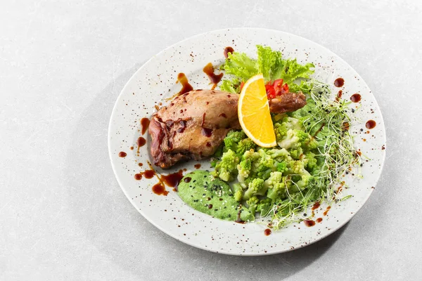 Roast duck leg with baked romanesco broccoli, lemon slice and chilli pepper on white plate, closeup. Horizontal view from above, top shot — Stock Photo, Image
