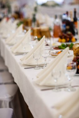 Lüks bir düğündeki masalar. Misafirler için bir masa. Tabaklar ve içecekler. Çiçek süsleme, beyaz sandalyeler ve masa. Düğün masası hazırlığı. Üst Manzara. Dikey fotoğraf