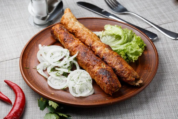 Shish kebab van gemalen rundvlees. Lula kebab met witte ui en salade, traditioneel Kaukasisch gerecht. Gelijnd op een mooie kleiplaat. horizontale foto. grijze achtergrond. bovenaanzicht. — Stockfoto