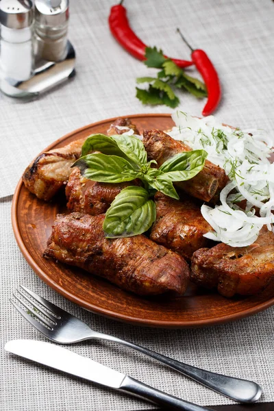 Gegrilde varkensribbetjes in bruine kleikom close-up. Vooraanzicht van de plaat met gegrilde varkensribben met ui en basilicum. Grijze achtergrond. verticale foto. Bovenaanzicht — Stockfoto