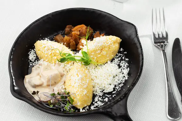 Typical Ukrainian dish polenta - Banosh with cheese, lard and white mushrooms. Maize porridge with bacon, cracklings and cheese. Corn porridge in black pan on white background. Horizontal photo. — Stock Photo, Image