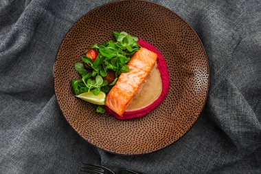 Pembe humus garnitürlü kızarmış balık fileto balığı. Kahverengi tabakta fırında somon ızgara limon, domates ve salata. Gri arka plan. Yatay fotoğraf.