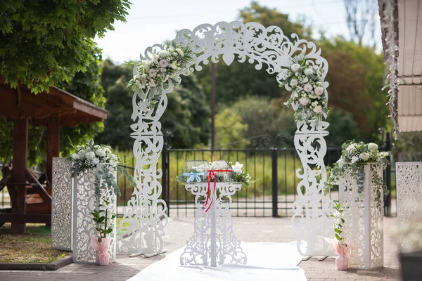 Wedding white wooden arch decorated with flowers outdoors. Beautiful wedding set up. Wedding ceremony on green lawn in the garden. Part of the festive decor, floral arrangement. Horizontal photo. — Stock Photo, Image