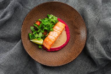 Pembe humus garnitürlü kızarmış balık fileto balığı. Kahverengi tabakta fırında somon ızgara limon, domates ve salata. Gri arka plan. Yatay fotoğraf.
