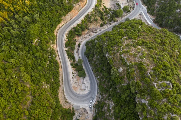 緑の森の真ん中に蛇紋岩の道のトップビュー。素晴らしい自然景観。空飛ぶドローンからの眺め。森の中の夏の緑の木と道路横写真. — ストック写真